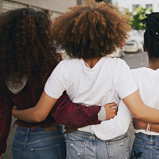 diverse young women from back with arms around each other diverse young women from back with arms around each other